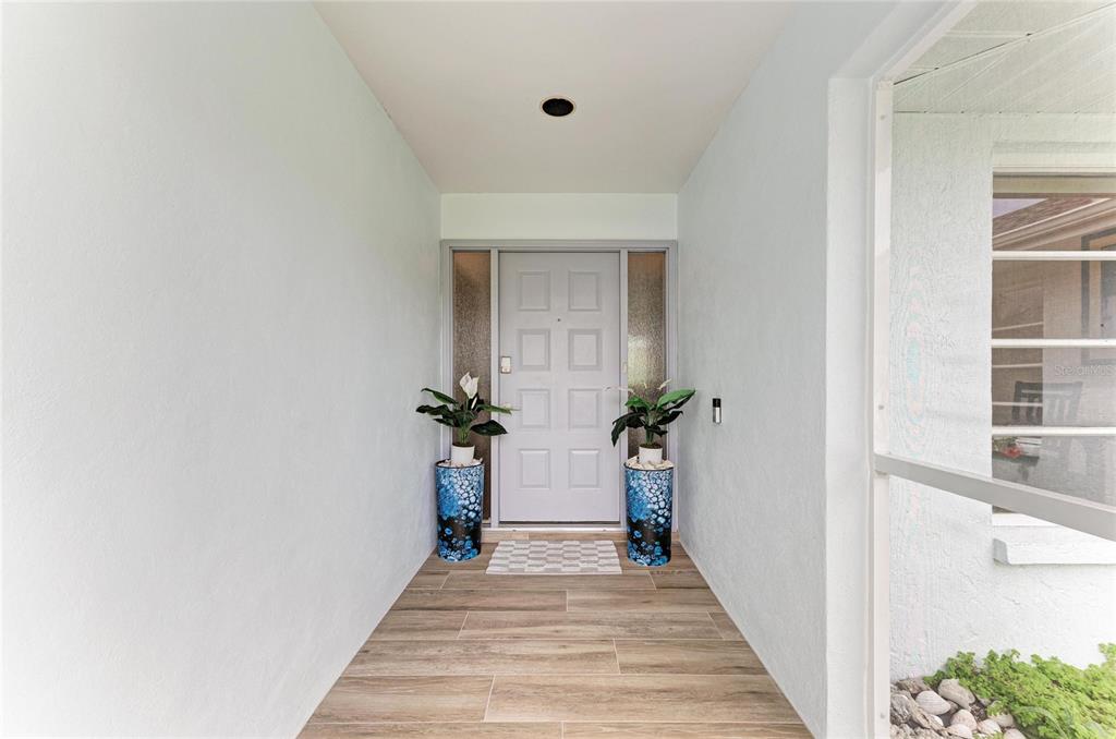 A covered entryway features a light-colored front door, tiled flooring, and two potted plants — 405 BAYSIDE LANE, NOKOMIS, FL