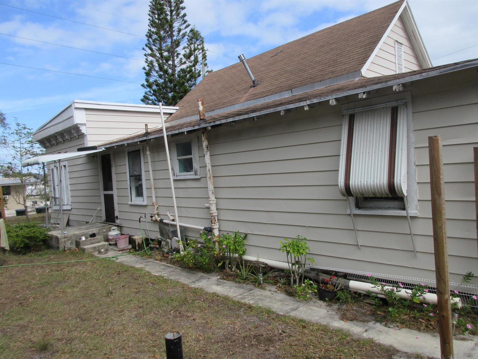 The exterior of a light-colored house features horizontal siding, a metal awning, and exposed pipes — 603 Avenue Avenue E, Fort Pierce FL 34950, FORT PIERCE, FL