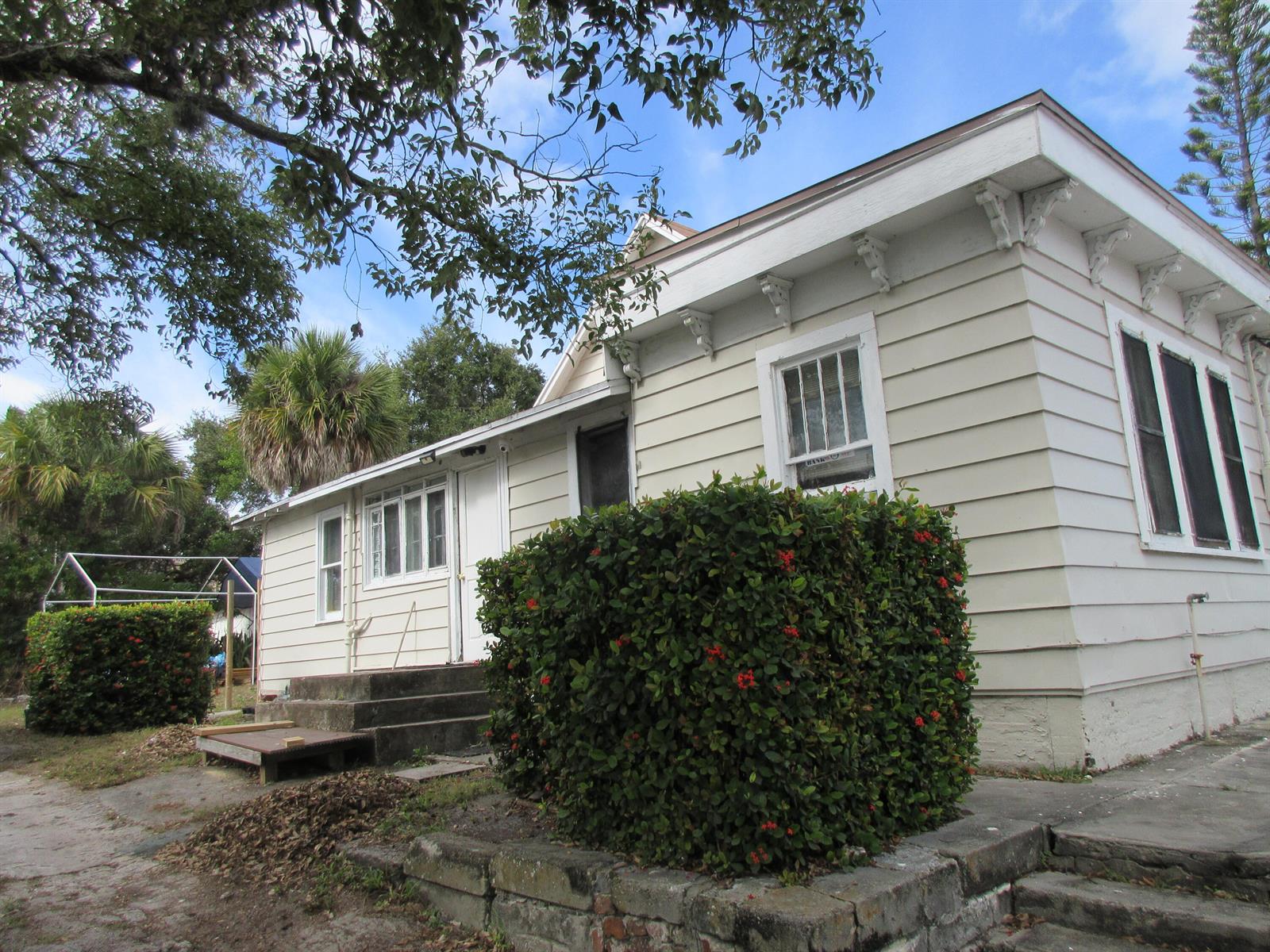 A light-colored, single-story house features horizontal siding, decorative roof brackets, and a large front hedge — 603 Avenue Avenue E, Fort Pierce FL 34950, FORT PIERCE, FL