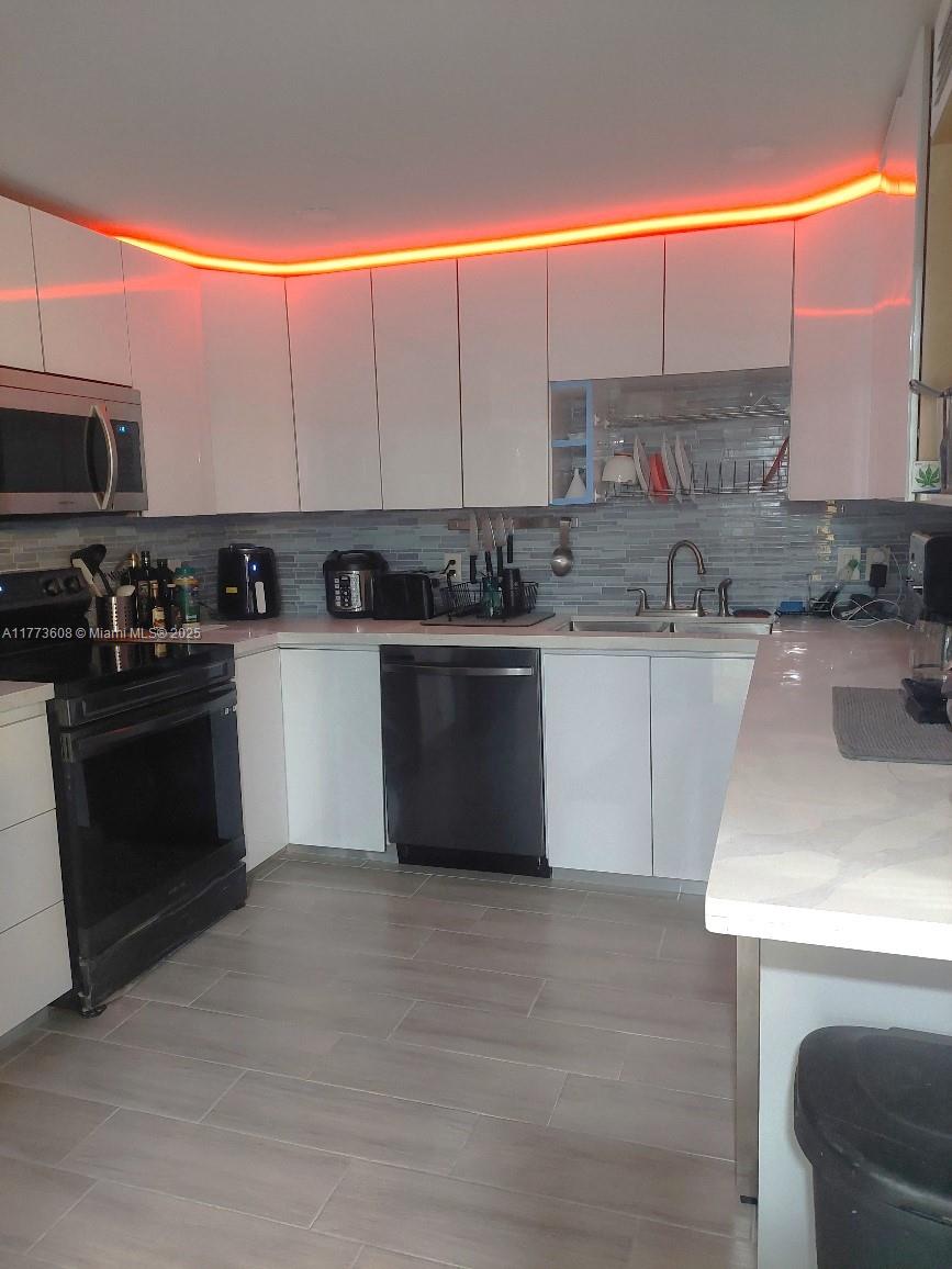 A kitchen features white cabinets, black appliances, a tiled backsplash, and orange under-cabinet lighting — 16300 Golf Club Rd Apt 317, Weston FL 33326, WESTON, FL
