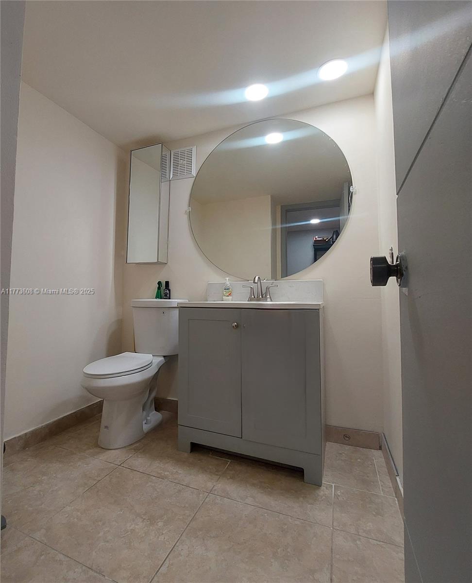 A bathroom features a gray vanity, a round mirror, and a white toilet on tile flooring — 16300 Golf Club Rd Apt 317, Weston FL 33326, WESTON, FL