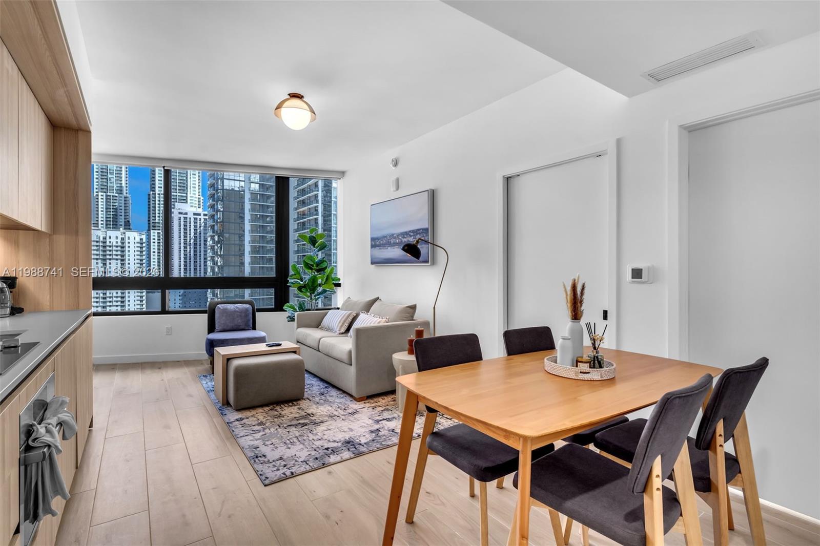 A modern living and dining area features light wood flooring, a sofa, and city views — 225 N Miami Ave # 1709, Miami FL 33131, MIAMI, FL
