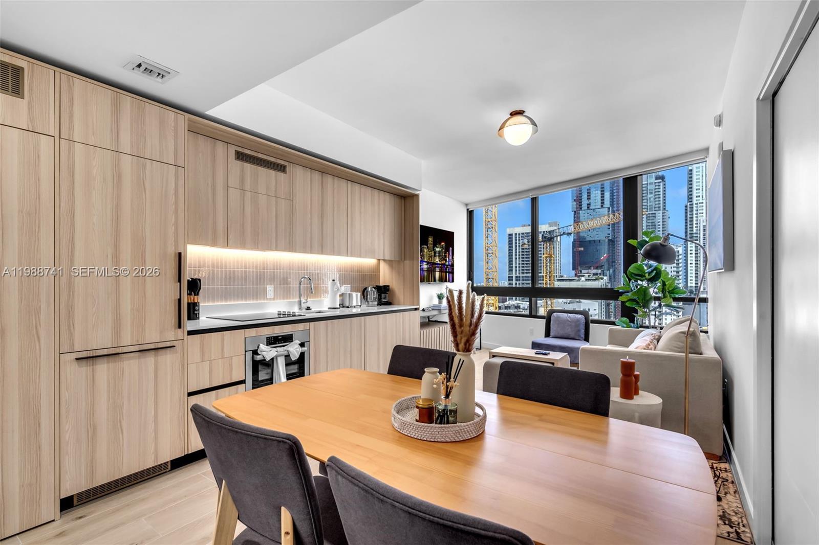 A modern kitchen and dining area features light wood cabinetry and floor-to-ceiling city windows — 225 N Miami Ave # 1709, Miami FL 33131, MIAMI, FL