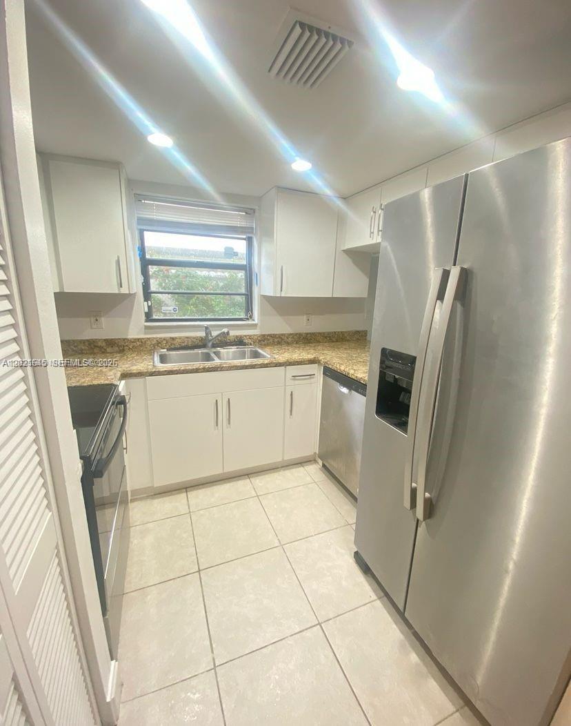 A kitchen features white cabinetry, stainless steel appliances, a double sink, and tiled flooring — MIAMI, FL