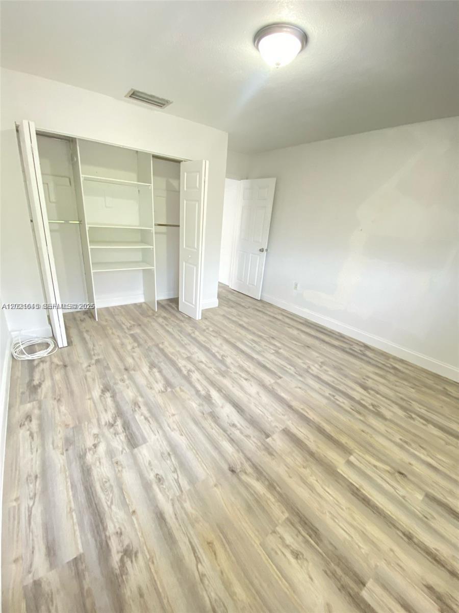 This bedroom features light wood-look flooring, white walls, and a built-in closet with shelving — MIAMI, FL