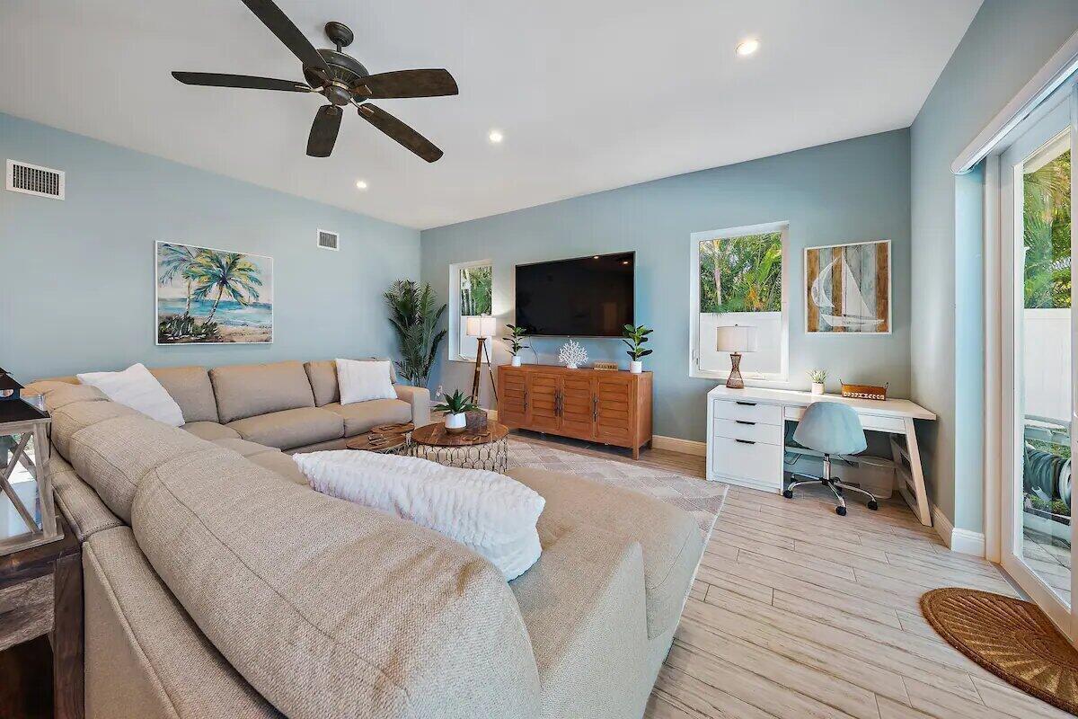 A living room features a sectional sofa, a television, and a desk on light flooring — 500 Sunrise Way, Juno Beach FL 33408, JUNO BEACH, FL