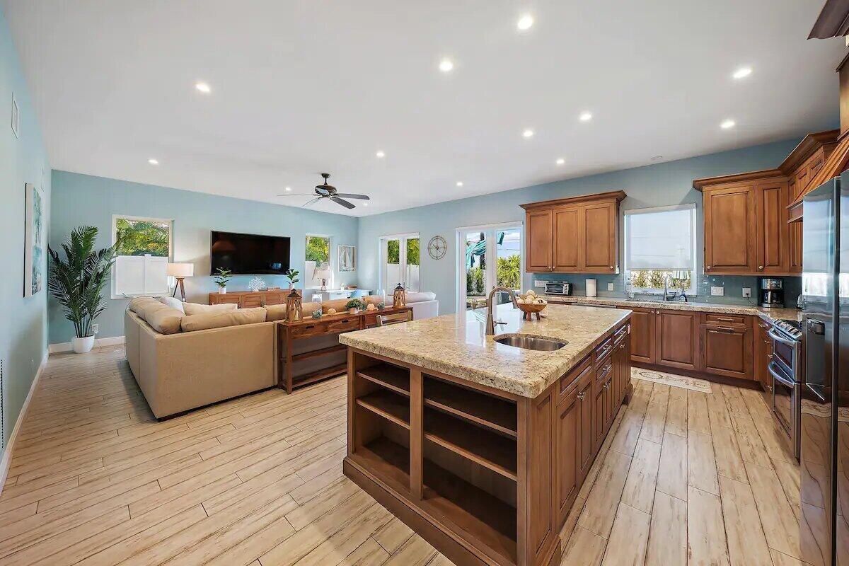An open-concept kitchen and living area featuring wood cabinets, granite countertops, and light flooring — 500 Sunrise Way, Juno Beach FL 33408, JUNO BEACH, FL