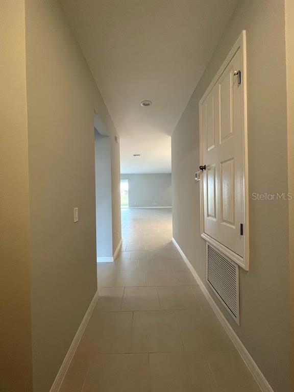 A hallway with light-colored tile flooring leads toward an open living area — 1415 GRASSLAND AVENUE, ST CLOUD, FL