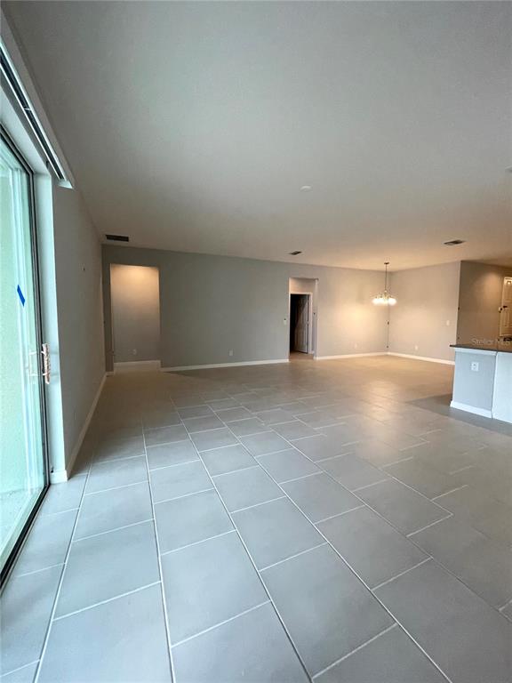 An open-concept living area features light gray tile flooring, neutral walls, and a sliding glass door — 1415 GRASSLAND AVENUE, ST CLOUD, FL