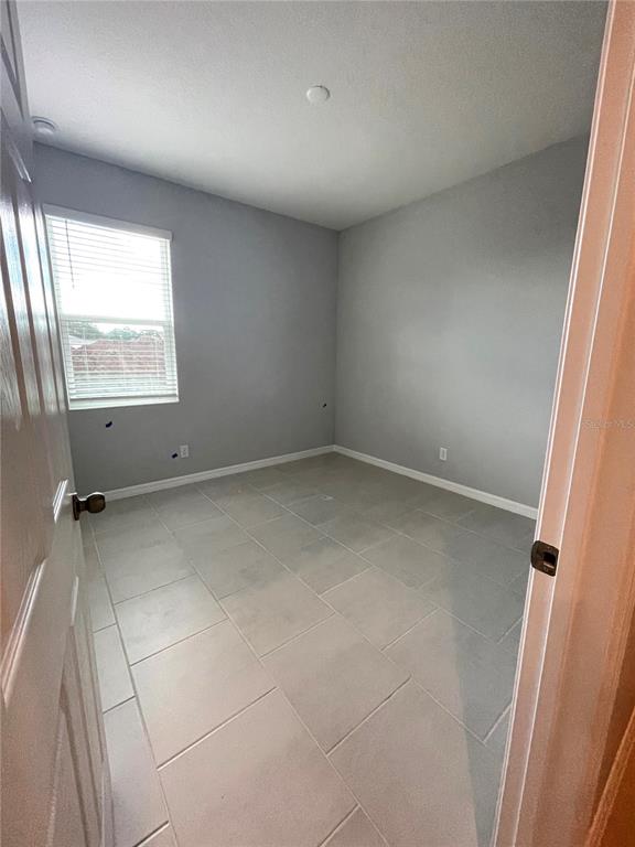 An empty bedroom features light gray walls, large beige floor tiles, and a window with blinds — 1415 GRASSLAND AVENUE, ST CLOUD, FL