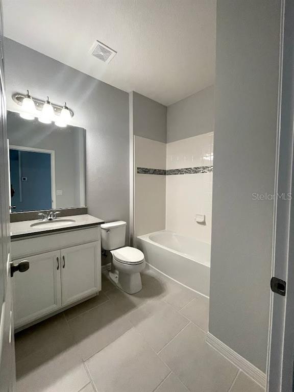 A bathroom features a vanity with a mirror, a toilet, and a tiled shower-tub combo — 1415 GRASSLAND AVENUE, ST CLOUD, FL