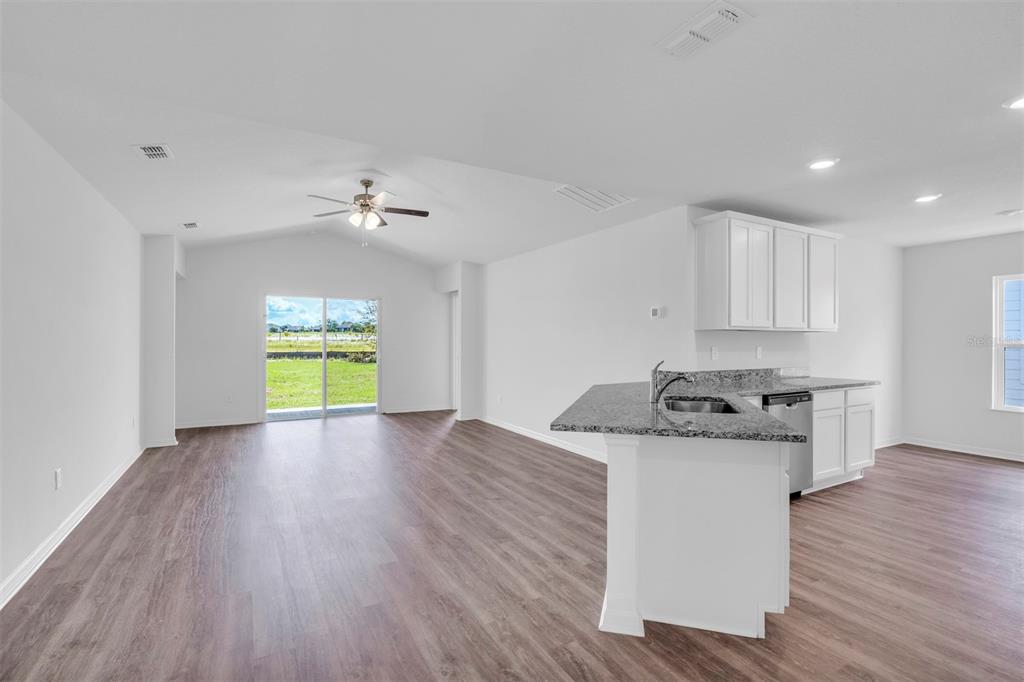 An open-concept kitchen and living area featuring white cabinets, granite countertops, and wood-look flooring — 13 PRINCE ANTHONY LANE, PALM COAST, FL