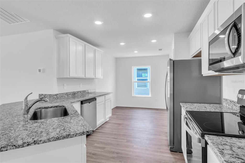 A modern kitchen features white cabinets, granite countertops, stainless steel appliances, and wood-look flooring — 13 PRINCE ANTHONY LANE, PALM COAST, FL