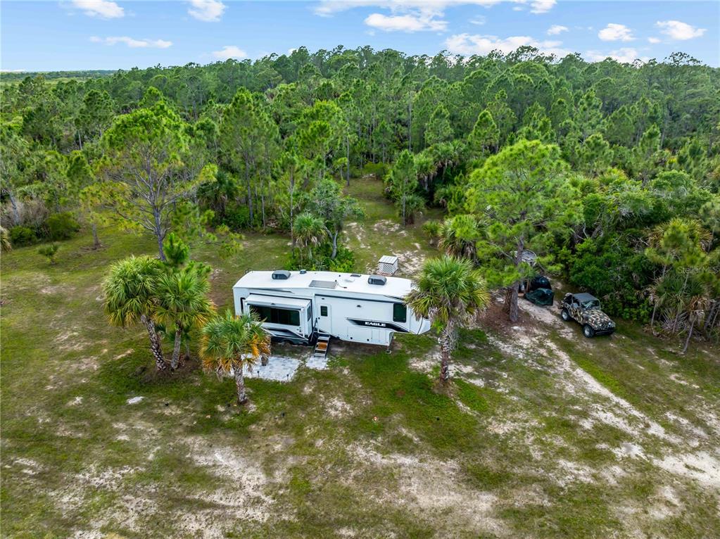 An aerial view shows a white fifth-wheel RV parked on a sandy lot near trees — 49909 BERMONT ROAD, PUNTA GORDA, FL