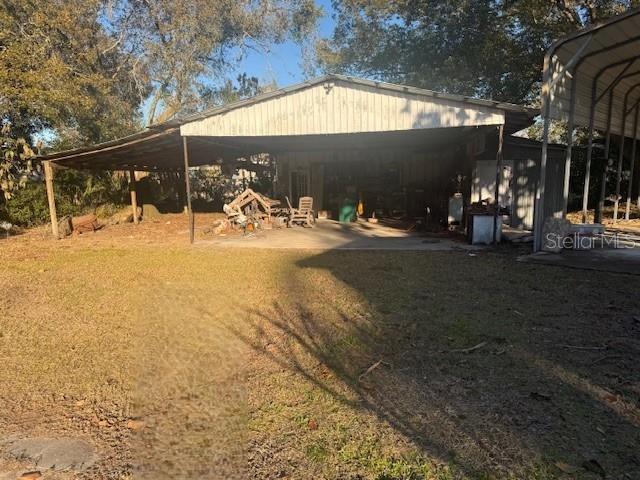 A large, open-sided metal carport stands on a grassy lot with trees in the background — 1813 DANIELS STREET, KISSIMMEE, FL