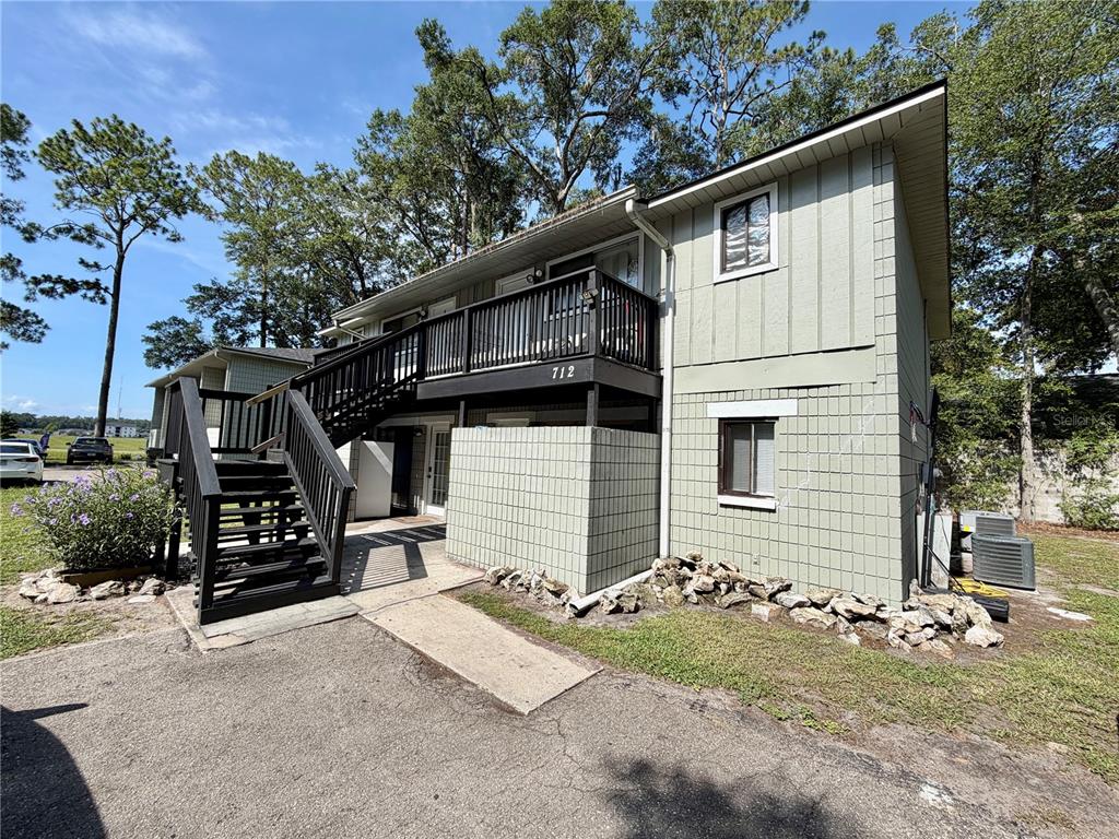 A two-story building with light green siding, a black wooden staircase, and a second-floor balcony — 712 SW 70TH TERRACE, GAINESVILLE, FL