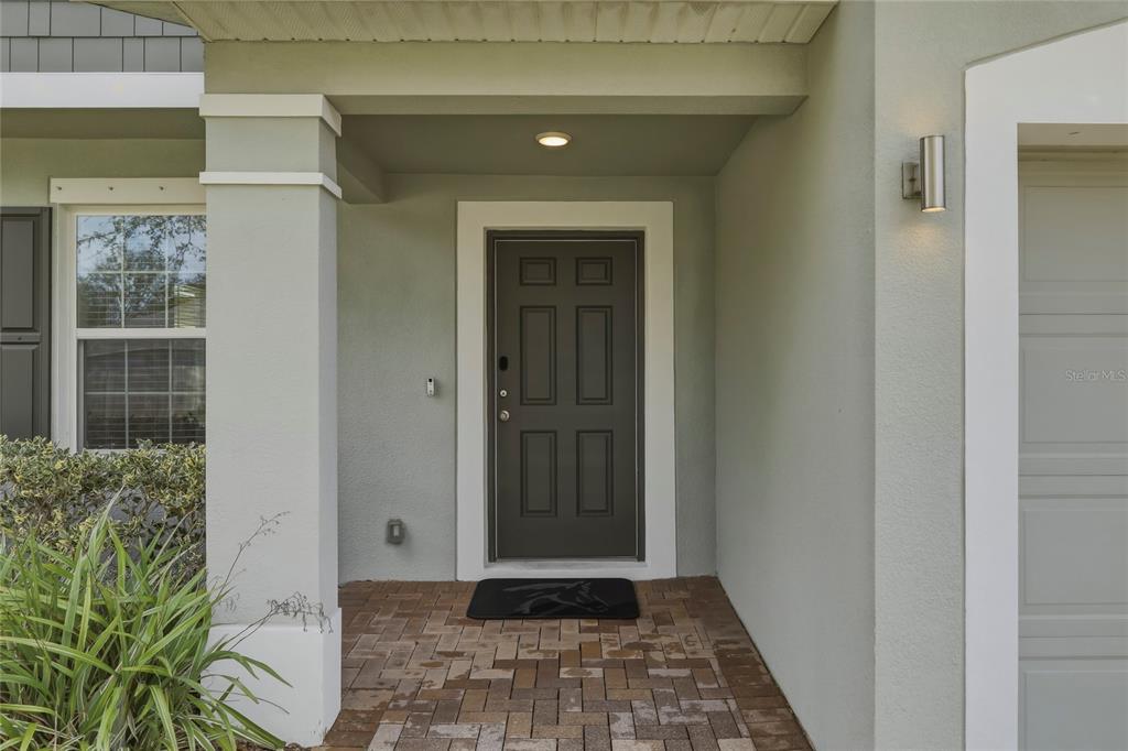 A covered entryway features a dark front door, brick pavers, and a light-colored exterior wall — 5573 REAGAN AVENUE, TITUSVILLE, FL