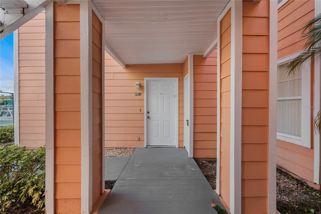 An exterior view of a residential building entrance with peach siding and a white door — 8709 ROCKINGHAM TERRACE UNIT A, KISSIMMEE, FL