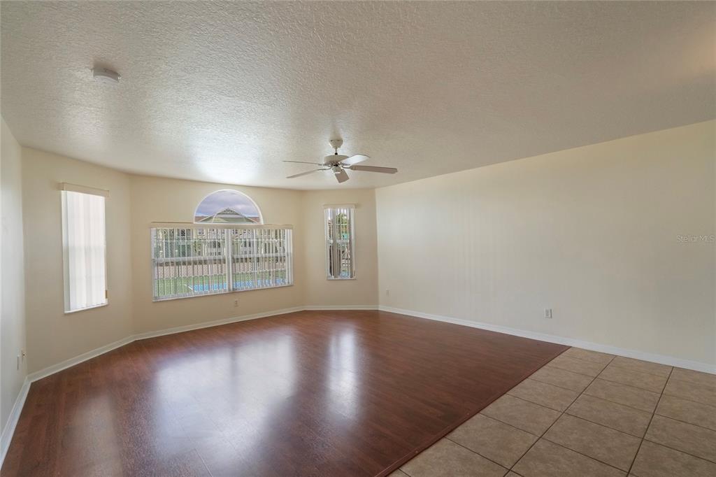 A spacious living room features wood-look flooring, a ceiling fan, and large windows with blinds — 8709 ROCKINGHAM TERRACE UNIT A, KISSIMMEE, FL