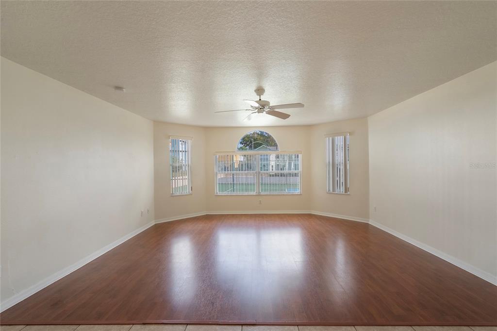 An empty living room features wood-look flooring, a ceiling fan, and a large bay window — 8709 ROCKINGHAM TERRACE UNIT A, KISSIMMEE, FL