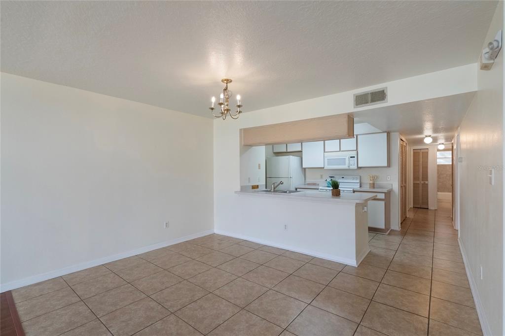 A dining area with tile flooring opens to a kitchen featuring white cabinets and appliances — 8709 ROCKINGHAM TERRACE UNIT A, KISSIMMEE, FL