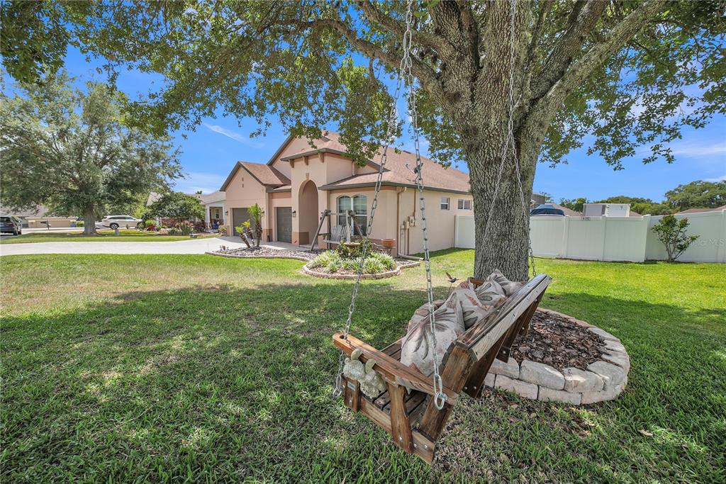 A wooden porch swing hangs from a large tree in the front yard of a house — 12309 LOOPBACK DRIVE, SAN ANTONIO, FL
