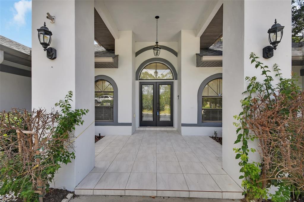 A covered entryway with white tile flooring leads to a dark-framed double front door — 2465 ROYAL ROAD, DELAND, FL
