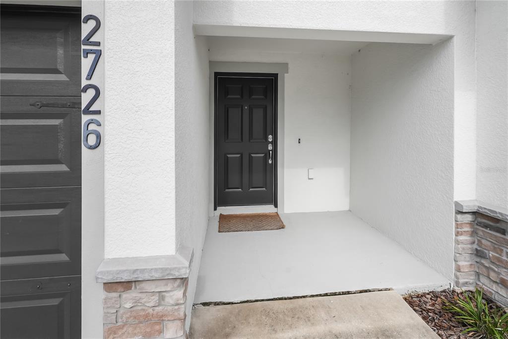 A black front door is recessed into a white exterior wall next to a garage — 2726 IDYLL LAKES CIRCLE, PLANT CITY, FL