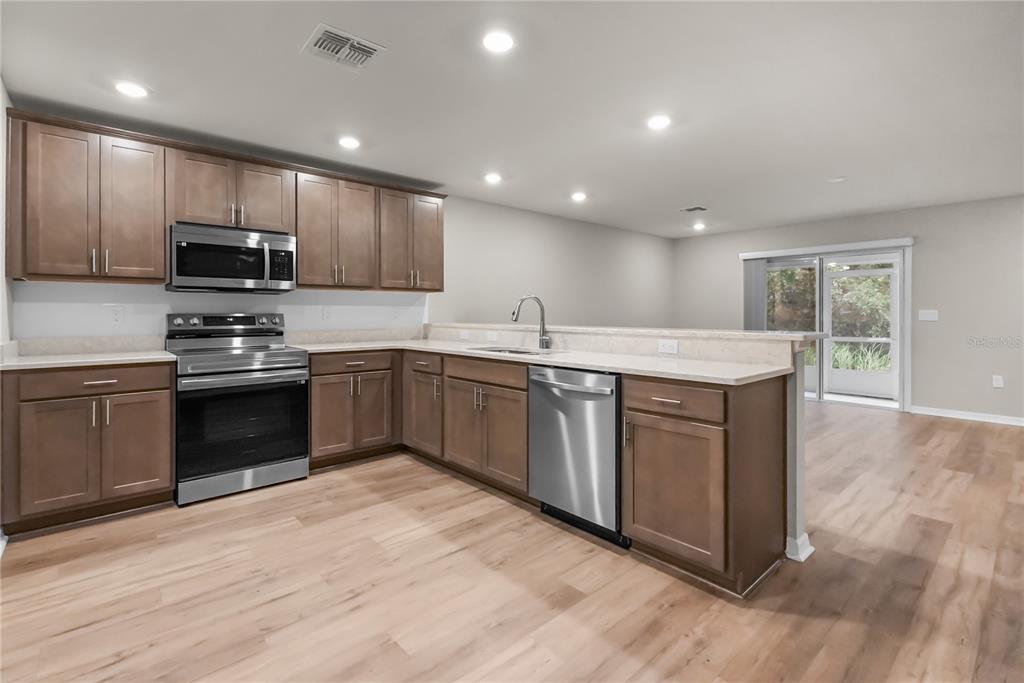 A kitchen with brown cabinets, stainless steel appliances, and light-colored countertops opens to a living area — 2726 IDYLL LAKES CIRCLE, PLANT CITY, FL