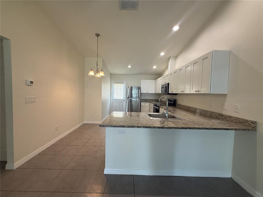 A kitchen features white cabinets, granite countertops, a stainless steel refrigerator, and tiled flooring — 350 W COURT STREET UNIT A, BUNNELL, FL