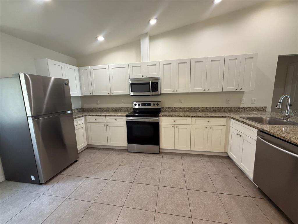 A kitchen features white cabinets, stainless steel appliances, and granite countertops over tile flooring — 350 W COURT STREET UNIT A, BUNNELL, FL