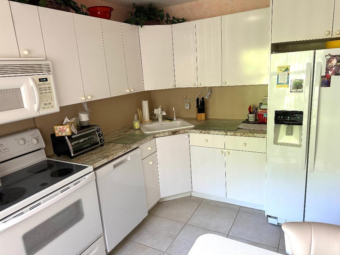 A kitchen features white cabinetry, granite countertops, a white appliance suite, and tile flooring — 8305 Casa Del Lago, Boca Raton FL 33433, BOCA RATON, FL