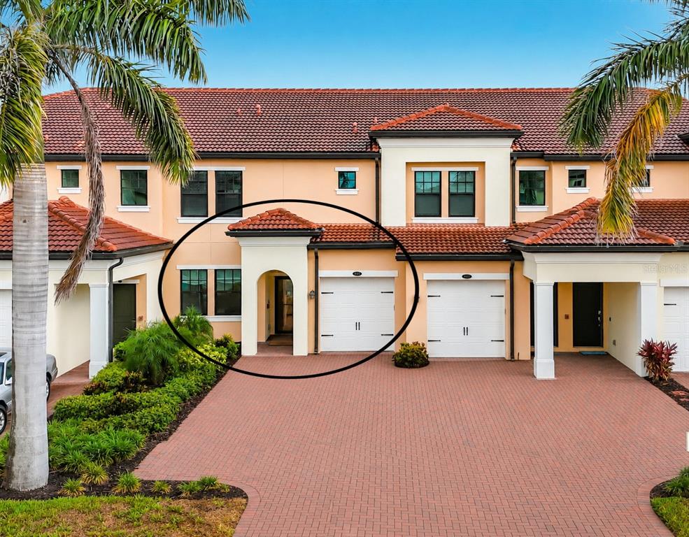 The exterior of a two-story townhouse featuring a brick driveway, arched entryway, and garage — 10051 CROOKED CREEK DRIVE UNIT 102, VENICE, FL