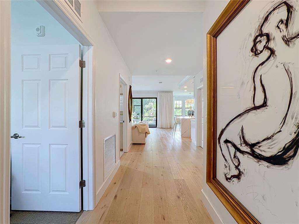 A hallway with light wood floors leads to an open-concept living area and kitchen — 10051 CROOKED CREEK DRIVE UNIT 102, VENICE, FL