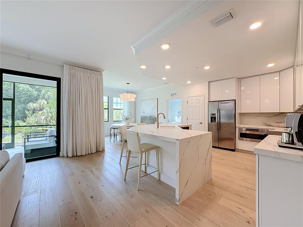 A modern kitchen features a marble waterfall island, white cabinetry, and light wood flooring — 10051 CROOKED CREEK DRIVE UNIT 102, VENICE, FL
