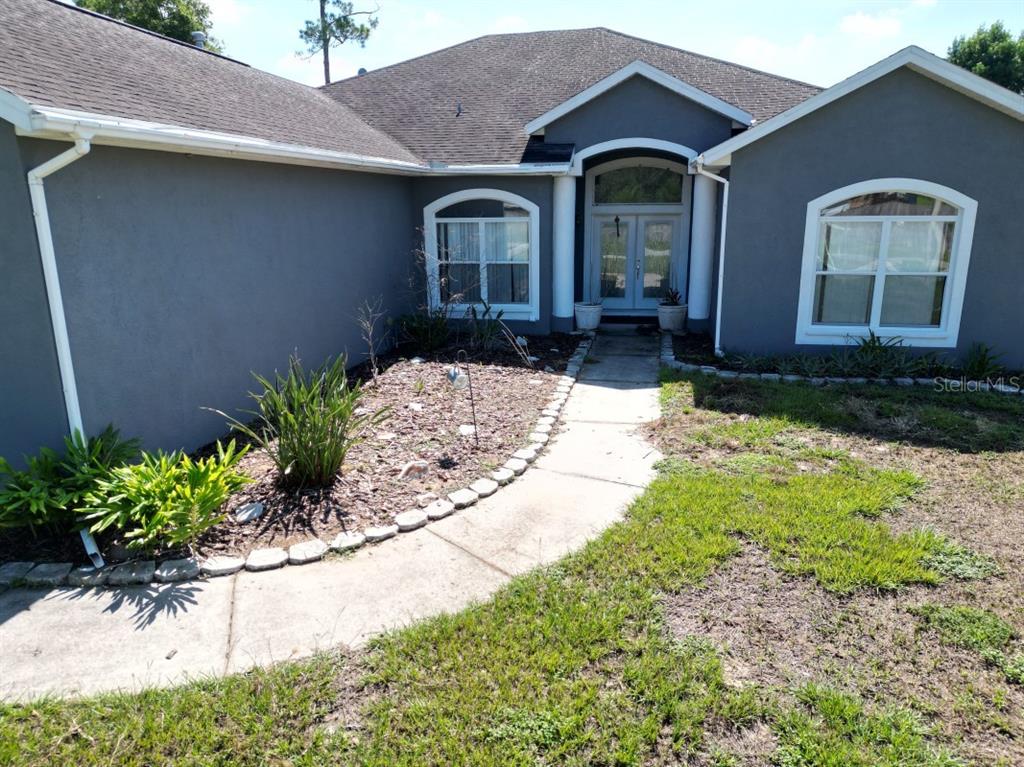 The exterior of a gray house features a curved walkway leading to a double-door entrance — 12106 PALM STREET, SAN ANTONIO, FL