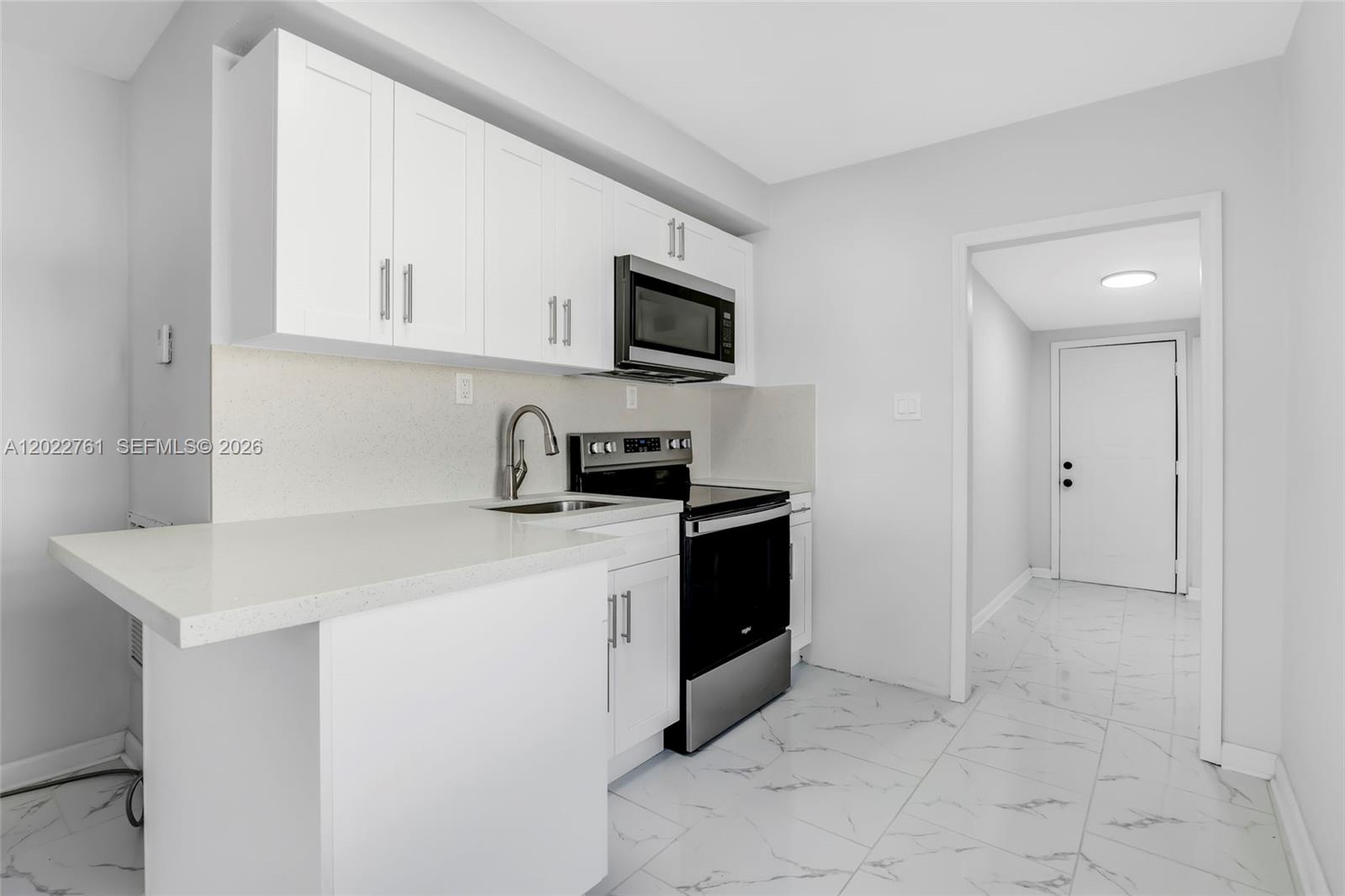 A kitchen features white cabinets, a black stove, a microwave, and white marble-patterned tile flooring — 6312 SW 19th St # 1, Miramar FL 33023, MIRAMAR, FL
