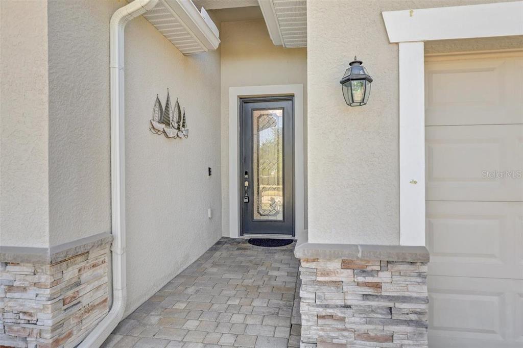 A stone-accented entryway features a dark-framed glass front door and a wall-mounted lantern light — 9481 RUSCELLO COURT, FORT MYERS, FL