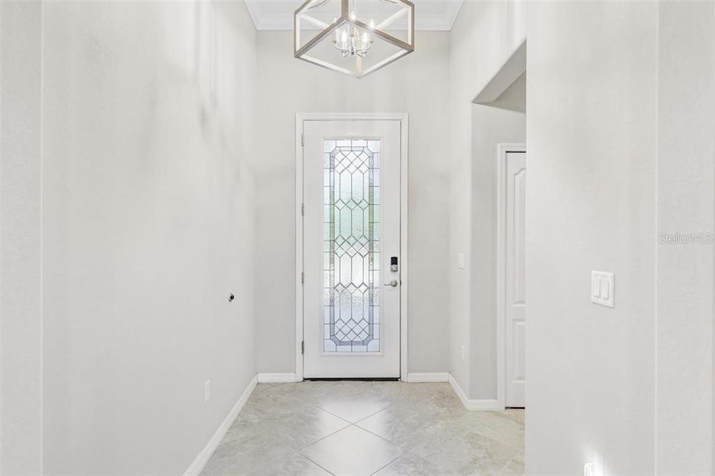 A bright entryway features a glass-paneled front door, tile flooring, and a modern geometric chandelier — 9481 RUSCELLO COURT, FORT MYERS, FL