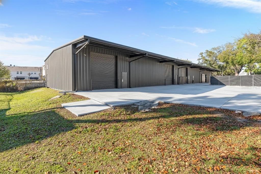 A modern, dark metal-sided industrial building features multiple roll-up doors and a concrete parking area — 220 E PALMETTO AVENUE, LONGWOOD, FL