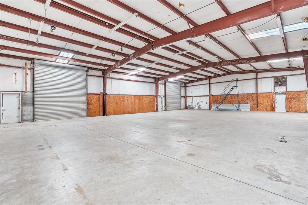 A large, empty industrial warehouse space features concrete floors, metal roll-up doors, and exposed beams — 220 E PALMETTO AVENUE, LONGWOOD, FL