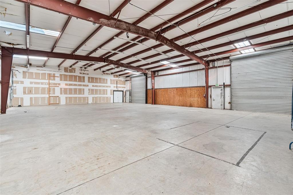 An empty industrial warehouse space features concrete floors, metal roll-up doors, and exposed steel beams — 220 E PALMETTO AVENUE, LONGWOOD, FL