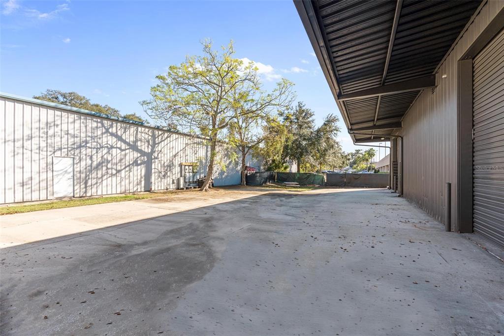 A concrete driveway sits between two metal industrial buildings under a clear blue sky — 220 E PALMETTO AVENUE, LONGWOOD, FL