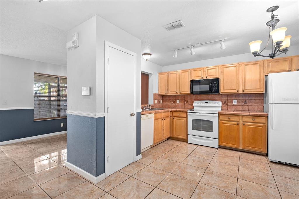 A kitchen with light wood cabinets, white appliances, and tiled floors next to a dining area — 2234 CYPRESS KNEE LOOP, KISSIMMEE, FL