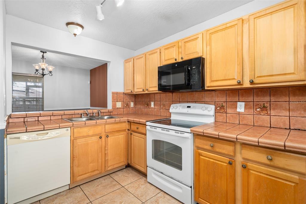 A kitchen features light wood cabinets, tiled countertops, and white appliances against a tiled backsplash — 2234 CYPRESS KNEE LOOP, KISSIMMEE, FL
