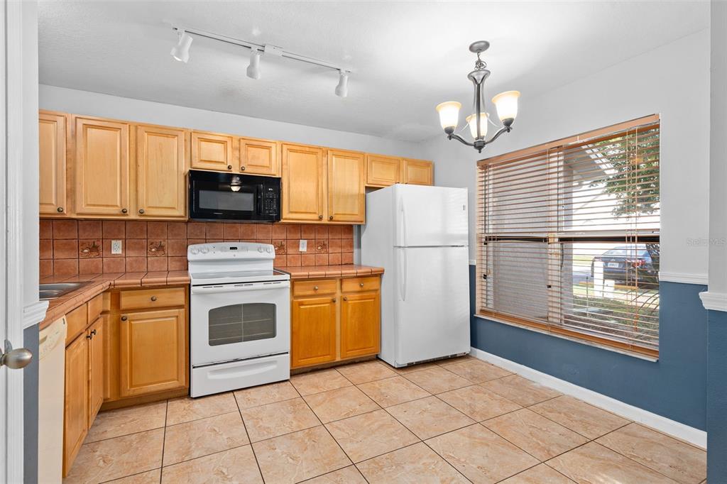 A kitchen with light wood cabinets, white appliances, tile countertops, and a dining area window — 2234 CYPRESS KNEE LOOP, KISSIMMEE, FL