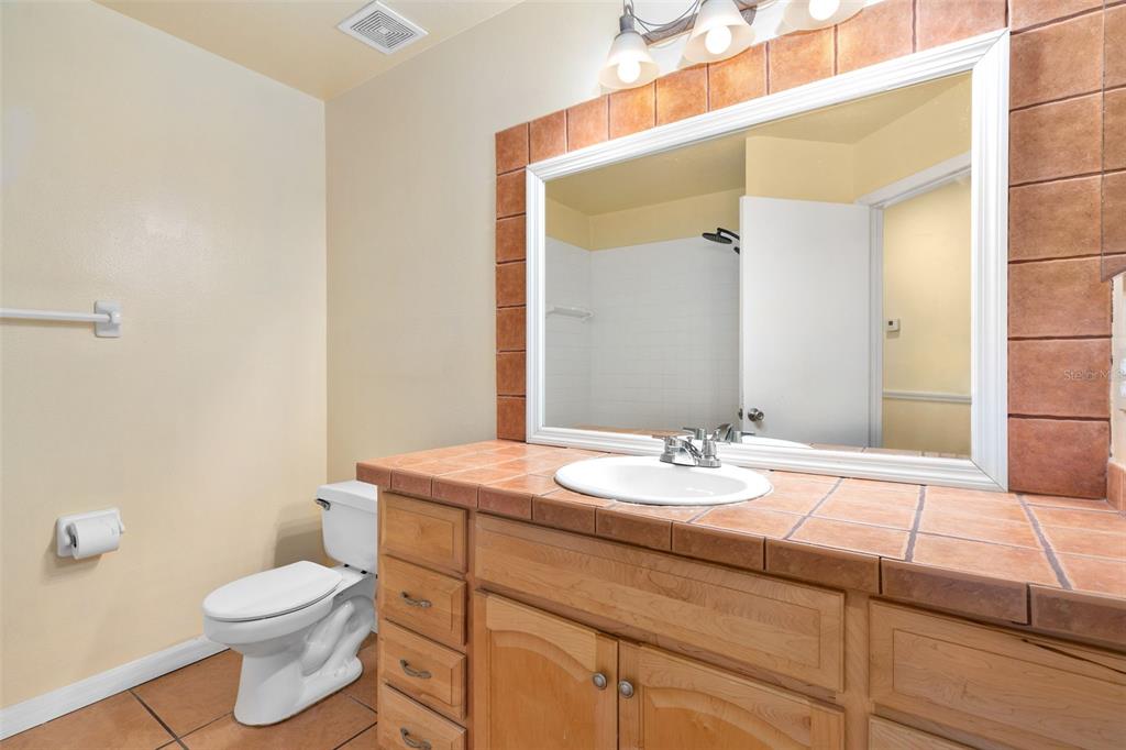 A bathroom features a tiled vanity countertop, wooden cabinets, a large mirror, and a toilet — 2234 CYPRESS KNEE LOOP, KISSIMMEE, FL