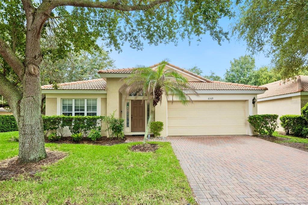 A single-story house with a tan stucco exterior, a tiled roof, and a brick driveway — 6169 FROGGATT STREET, ORLANDO, FL
