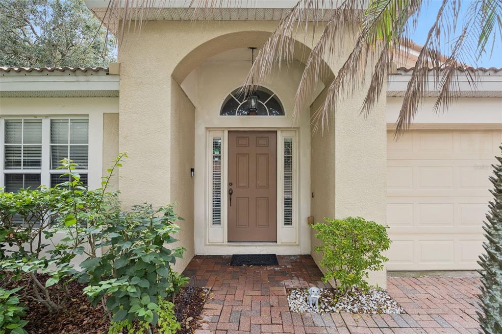 The exterior of a house features a tan stucco facade, a brown front door, and brick pavers — 6169 FROGGATT STREET, ORLANDO, FL