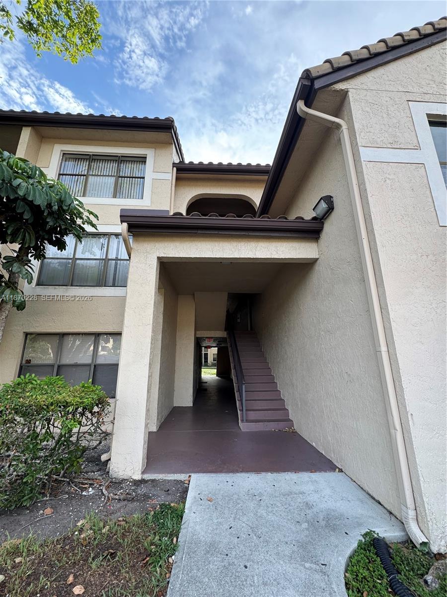 An exterior view of a multi-story apartment building with a covered staircase and stucco walls — 4341 W McNab Rd # 27, Pompano Beach FL 33069, POMPANO BEACH, FL